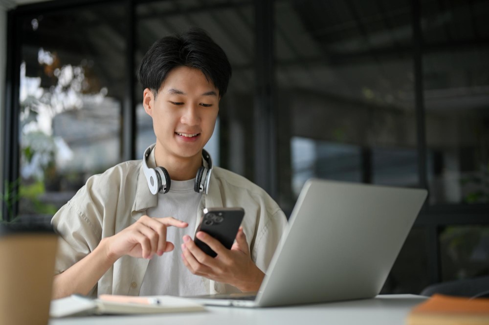 Nam nhân viên trẻ đang sử dụng điện thoại và laptop để cải thiện hình ảnh cá nhân trên mạng xã hội