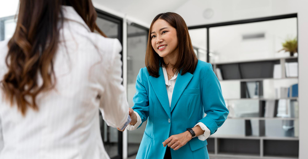 Two female office workers shaking hands in the office and smiling with each other