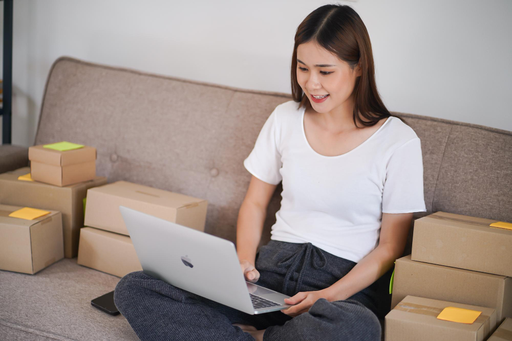Young woman sitting on a sofa with a laptop, typing a confirm meeting appointment email for her business.