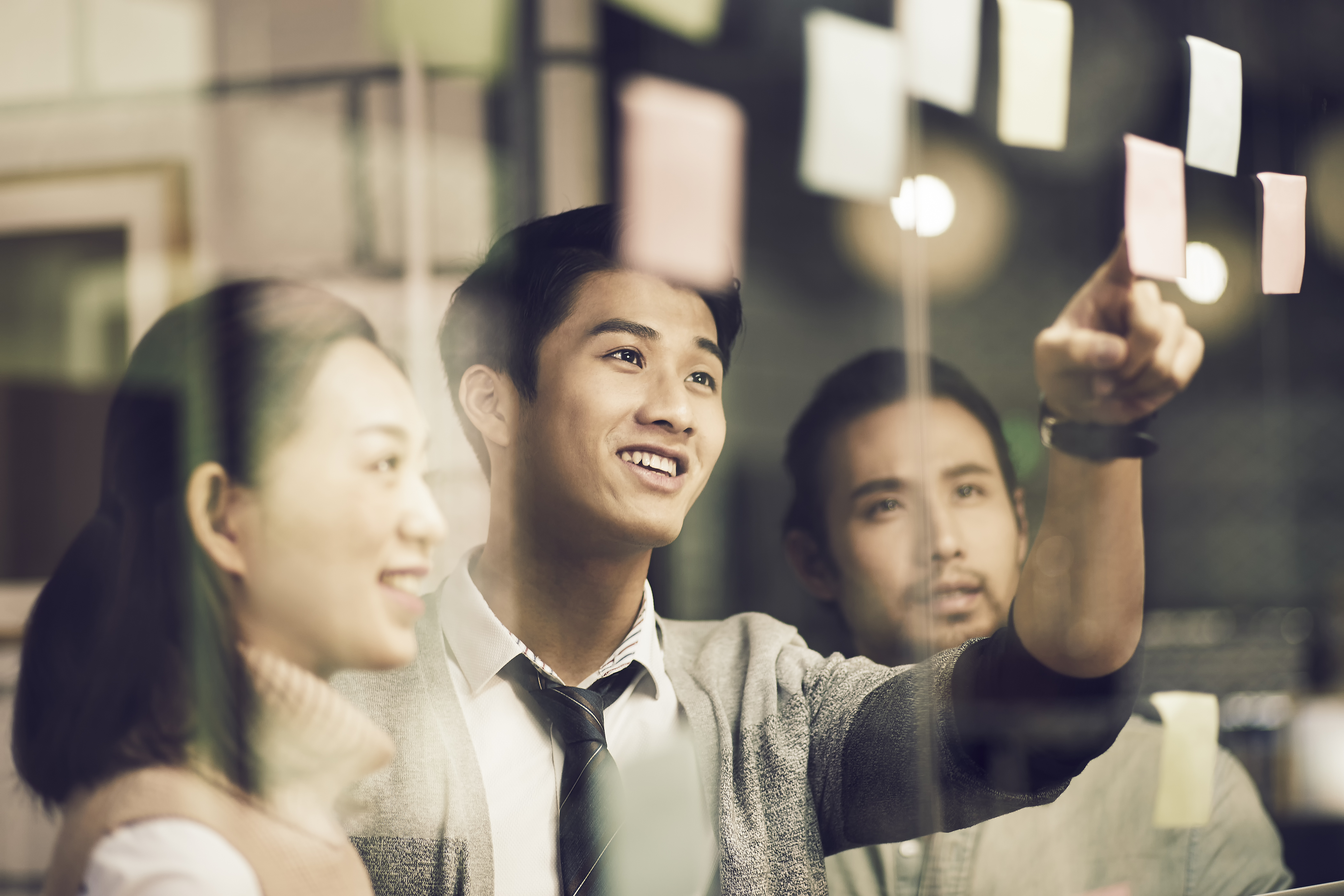 Nhóm nhân viên trẻ nhìn vào tường ghi chú thảo luận công việc.