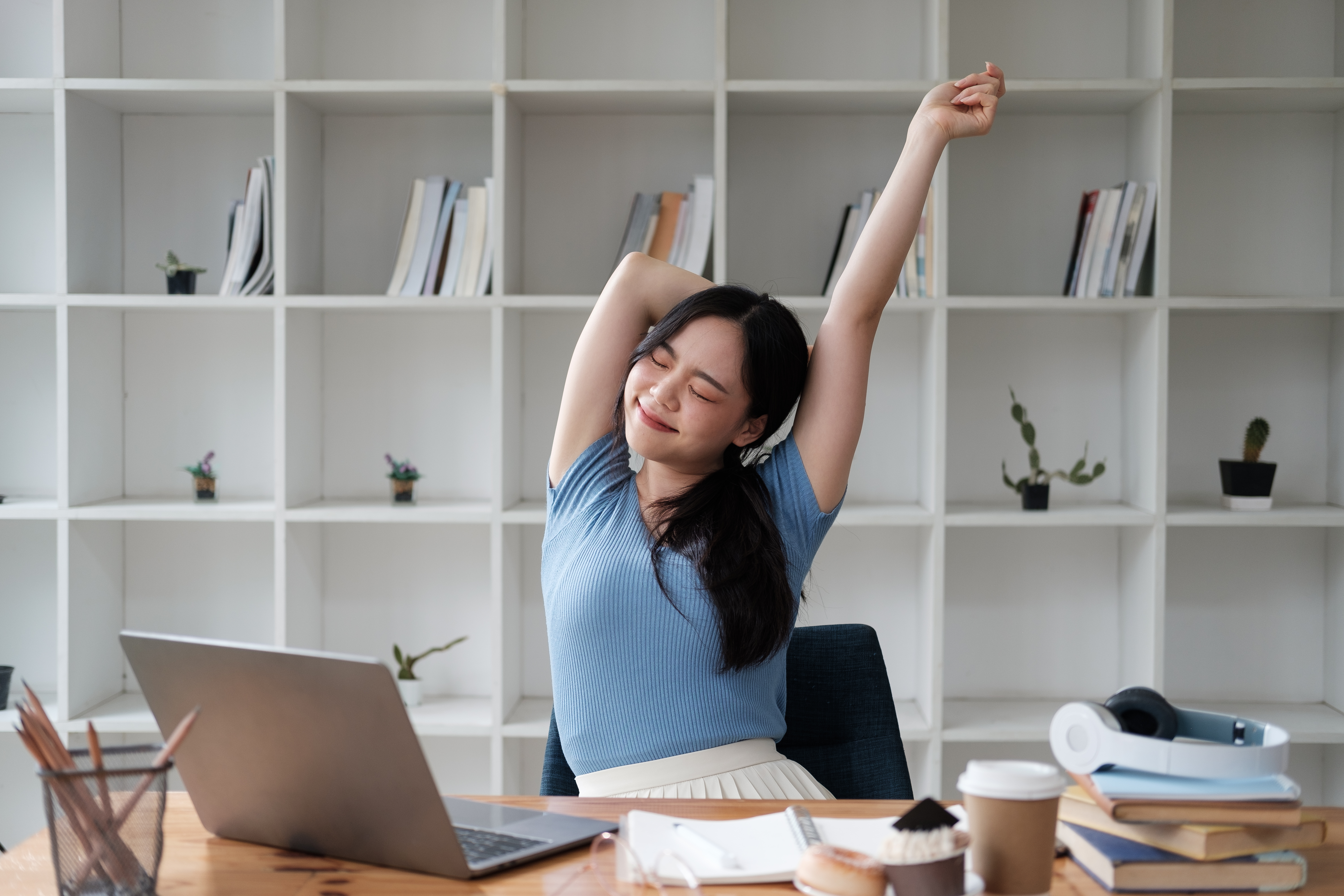 A woman enjoying a balanced work from home job, stretching at a home office desk.