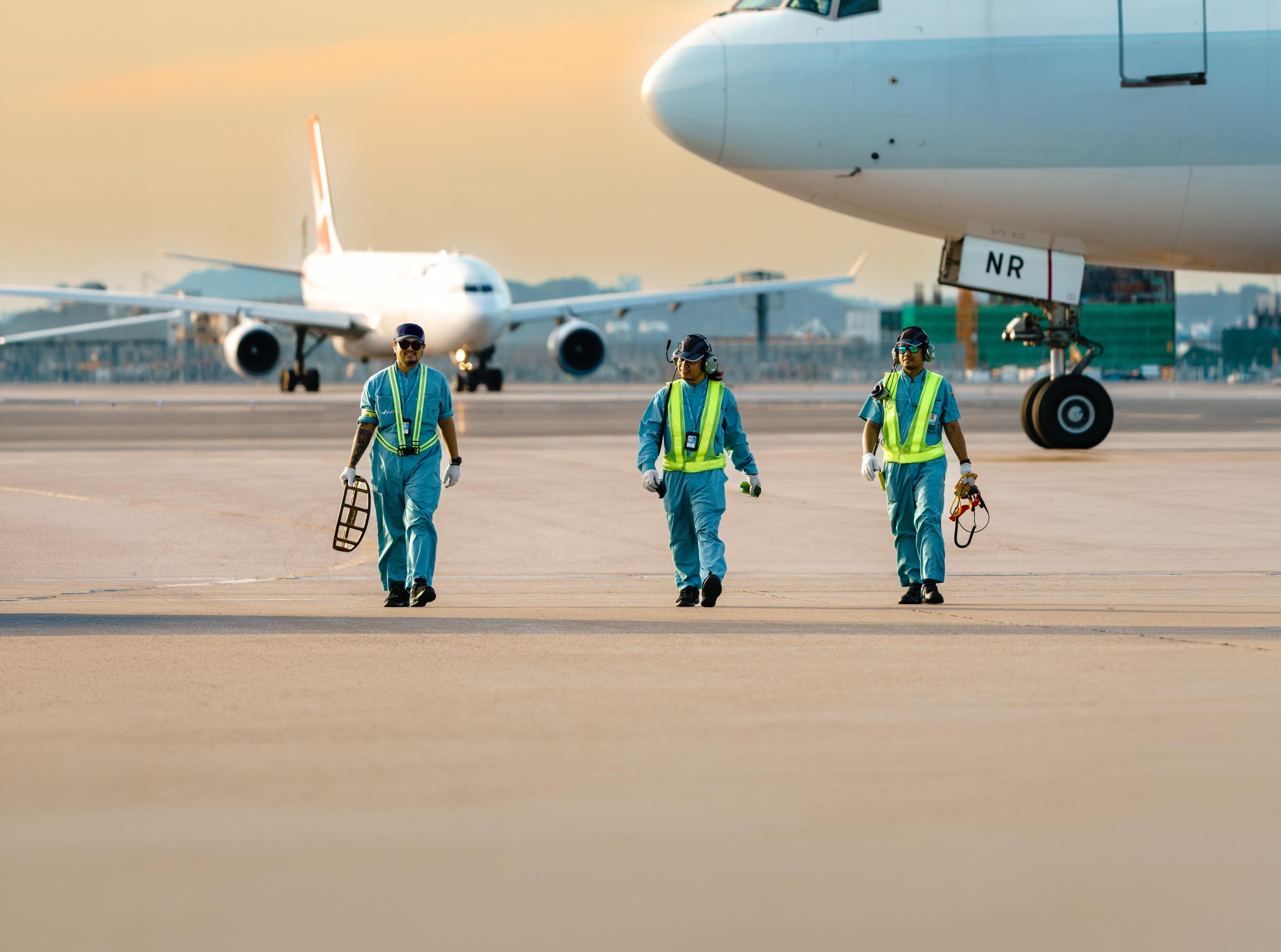 3 aircraft engineers walk in the sunset at a hangar of HAECO