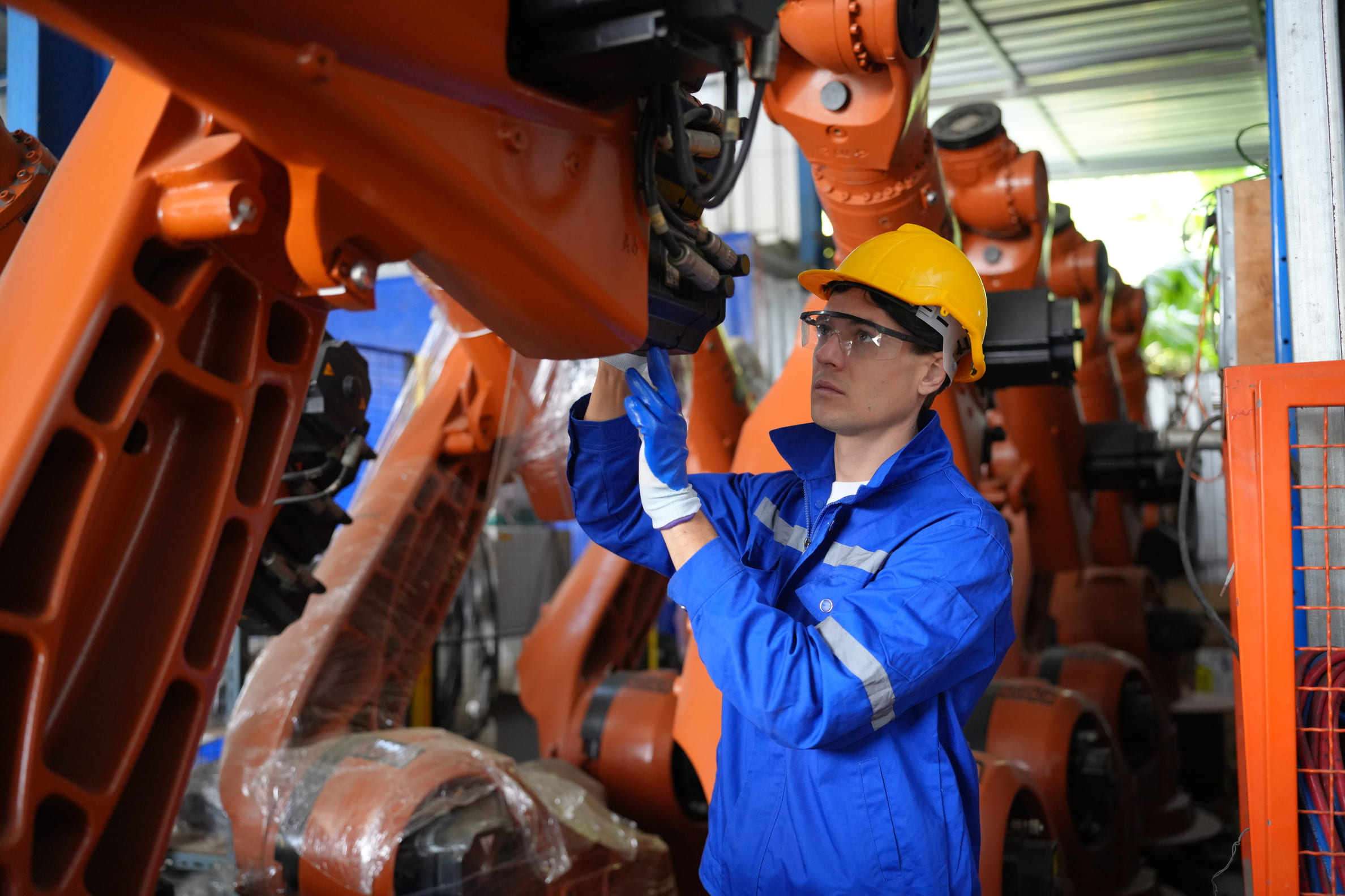 Kỹ thuật viên công nghiệp vận hành máy điều khiển bên cạnh cánh tay robot tự động trên dây chuyền sản xuất