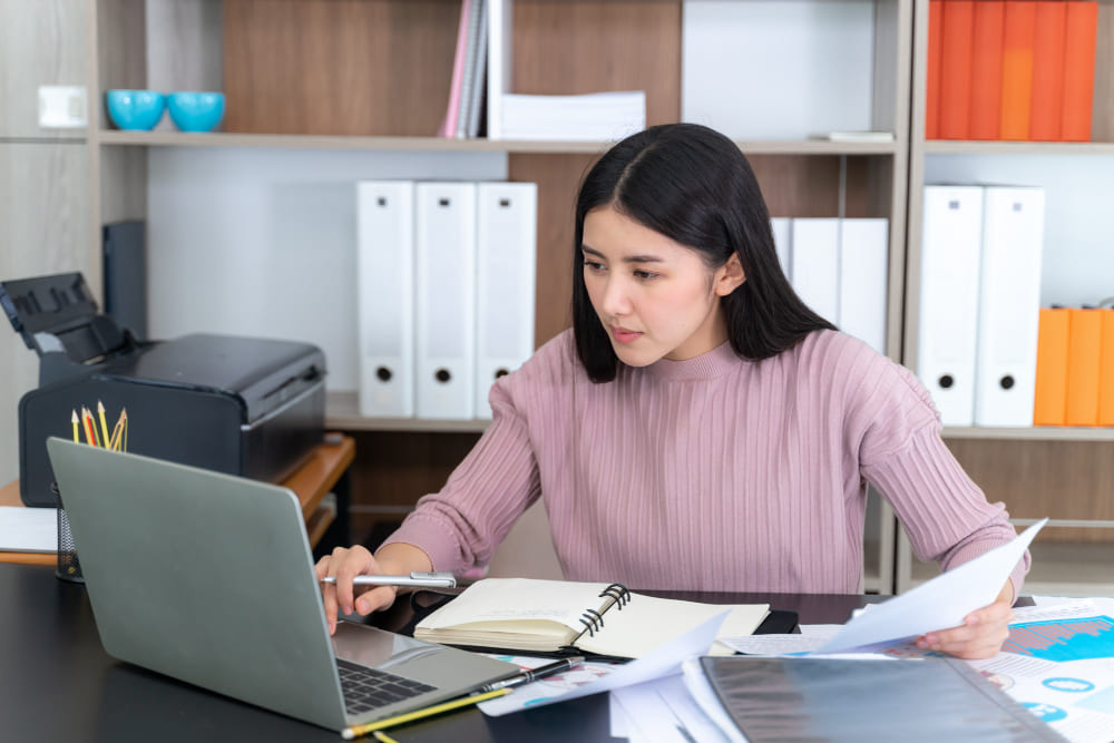 Finance administrator reviewing paper receipts and digital expense claims at an office workstation