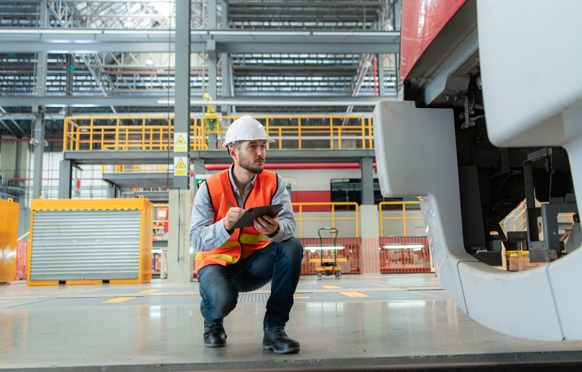 Maintenance technician using a digital tablet to inspect automated equipment on a factory floor