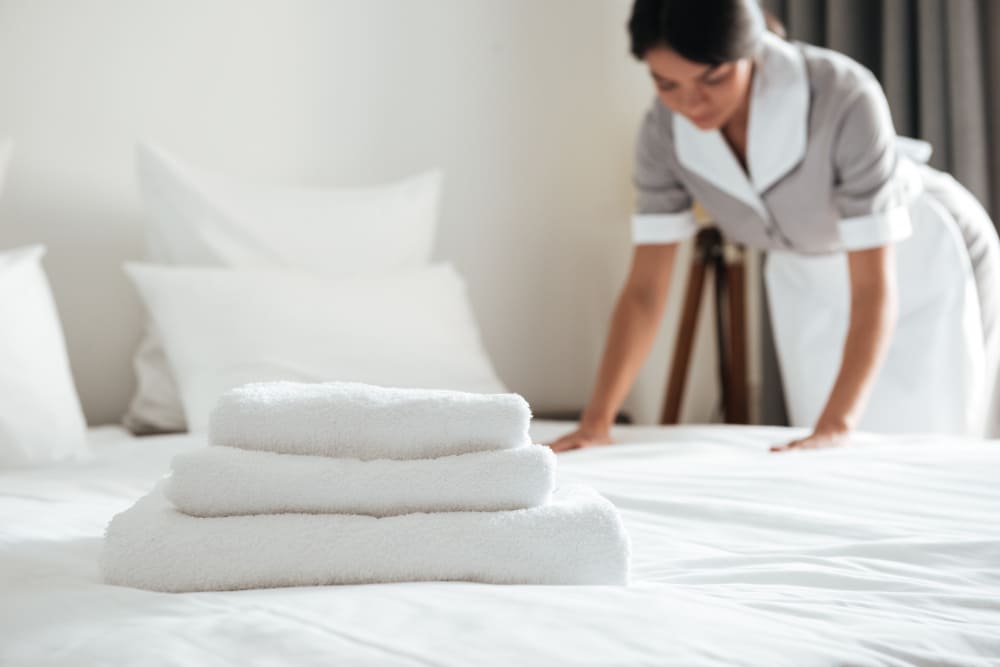 Hotel housekeeper preparing a guest room with fresh linens in a modern hotel.